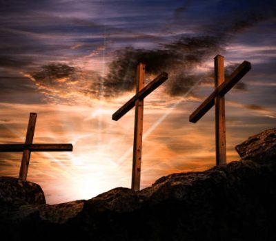 Silhouette of three wooden crosses above the hill with dramatic sky and sun rays at sunset. Religious symbol of good friday
